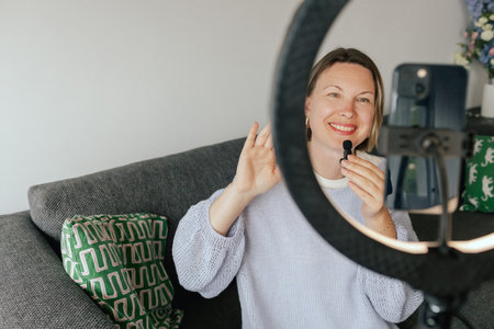 Middle-aged woman beauty blogger filming skincare product unboxing at home with ring light. User-generated content UGC for online store promotion. Vlogger live streaming. Part of a seriesの写真素材