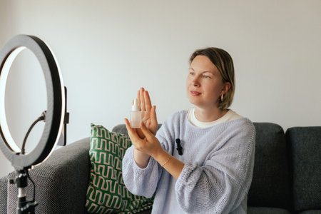 Middle-aged woman beauty blogger filming skincare product unboxing at home with ring light....