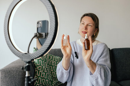 Middle-aged woman beauty blogger filming skincare product unboxing at home with ring light. User-generated content UGC for online store promotion. Vlogger live streaming. Part of a seriesの写真素材