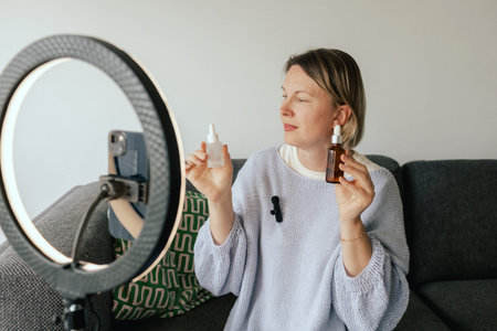 Middle-aged woman beauty blogger filming skincare product unboxing at home with ring light. User-generated content UGC for online store promotion. Vlogger live streaming. Part of a seriesの写真素材