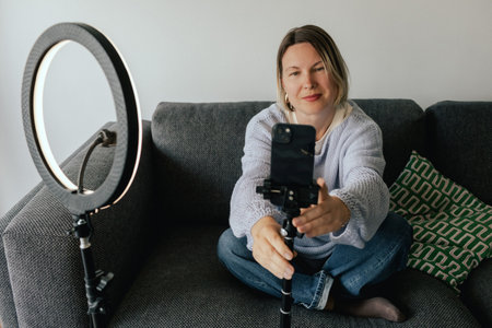 Middle-aged woman beauty blogger filming skincare product unboxing at home with ring light. User-generated content UGC for online store promotion. Vlogger live streaming. Part of a seriesの写真素材