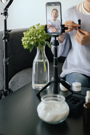 Middle-aged woman beauty blogger filming skincare product unboxing at home with ring light. User-generated content UGC for online store promotion. Vlogger live streaming. Part of a seriesの写真素材