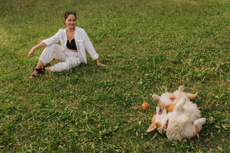 Young girl trains Welsh Corgi in the park in sunny weather. Concept of walking a dog, friendship between a dog and owner. Part of a series. Soft focus.の写真素材