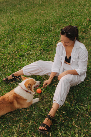 Young girl trains Welsh Corgi in the park in sunny weather. Concept of walking a dog, friendship between a dog and owner. Part of a series. Soft focus.の写真素材
