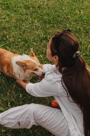 Close-up of a woman hugging a Welsh Corgi in the park in sunny weather. Concept of walking a dog, friendship between a dog and owner. Part of a series. Soft focus.の写真素材
