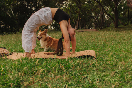 Fit sporty mindful young woman meditating, doing yoga and breathing exercises with eyes closed, feeling peace and balance in tropical park with her Corgi dog on a sunny day.の写真素材