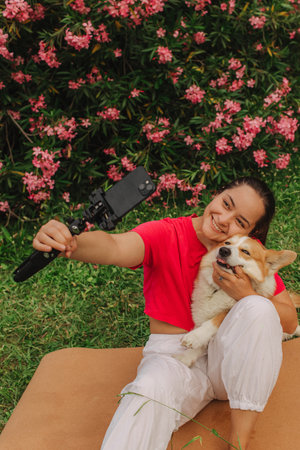 Young girl with Corgi recording video on phone share via app her travel vacation. Gen Z influencer shooting social media stories. Concept of friendship between a dog and human. Part of a series. UGCの写真素材