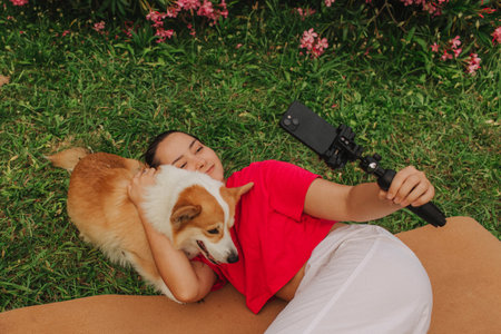 Young girl with Corgi recording video on phone share via app her travel vacation. Gen Z influencer shooting social media stories. Concept of friendship between a dog and human. Part of a series. UGCの写真素材