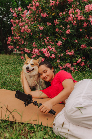 Young girl with Corgi recording video on phone share via app her travel vacation. Gen Z influencer shooting social media stories. Concept of friendship between a dog and human. Part of a series. UGCの写真素材