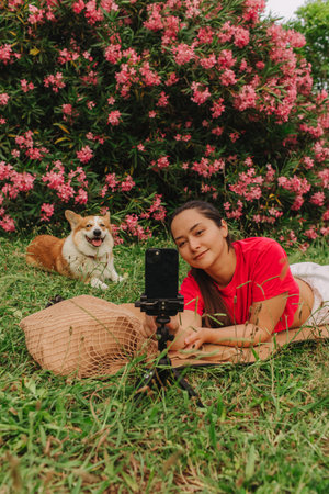 Young girl with Corgi recording video on phone share via app her travel vacation. Gen Z influencer shooting social media stories. Concept of friendship between a dog and human. Part of a series. UGCの写真素材