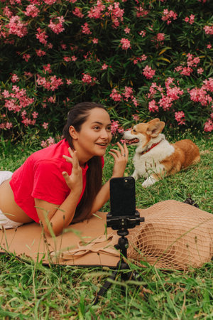 Young girl with Corgi recording video on phone share via app her travel vacation. Gen Z influencer shooting social media stories. Concept of friendship between a dog and human. Part of a series. UGCの写真素材