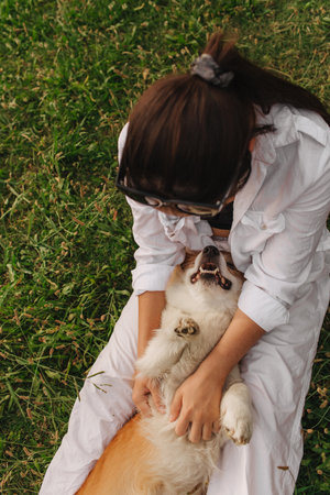 Close-up of a woman hugging a Welsh Corgi in the park in sunny weather. Concept of walking a dog, friendship between a dog and owner. Part of a series. Soft focus.の写真素材