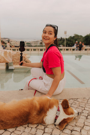 Young girl with Corgi recording video on phone share via app her travel vacation. Gen Z influencer shooting social media stories. Concept of friendship between a dog and human. Part of a series. UGCの写真素材