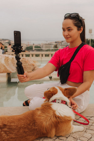 Young girl with Corgi recording video on phone share via app her travel vacation. Gen Z influencer shooting social media stories. Concept of friendship between a dog and human. Part of a series. UGCの写真素材
