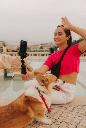 Young girl with Corgi recording video on phone share via app her travel vacation. Gen Z influencer shooting social media stories. Concept of friendship between a dog and human. Part of a series. UGCの写真素材