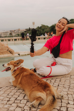 Young girl with Corgi recording video on phone share via app her travel vacation. Gen Z influencer shooting social media stories. Concept of friendship between a dog and human. Part of a series. UGCの写真素材