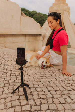 Young girl with Corgi recording video on phone share via app her travel vacation. Gen Z influencer shooting social media stories. Concept of friendship between a dog and human. Part of a series. UGCの写真素材