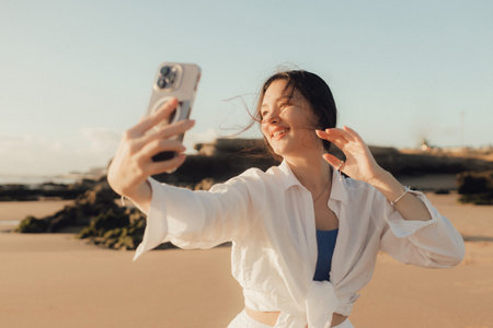 Young girl recording video on phone share via app her travel vacation near seaside. Gen Z influencer shooting social media stories. Concept of solo tourism and sustainable lifestyle. Part of a series. UGCの写真素材