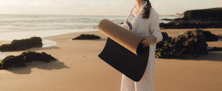 Asian happy woman in white clothes with yoga mat on the ocean shore. Concept of health exercises and yoga. Tourism alone. Part of series.の写真素材