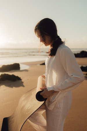 Asian happy woman in white clothes with yoga mat on the ocean shore. Concept of health exercises and yoga. Tourism alone. Part of series.の写真素材
