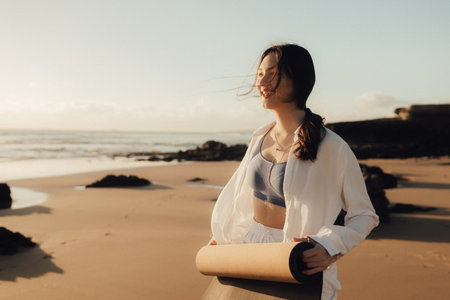 Asian happy woman in white clothes with yoga mat on the ocean shore. Concept of health exercises and yoga. Tourism alone. Part of series.の写真素材