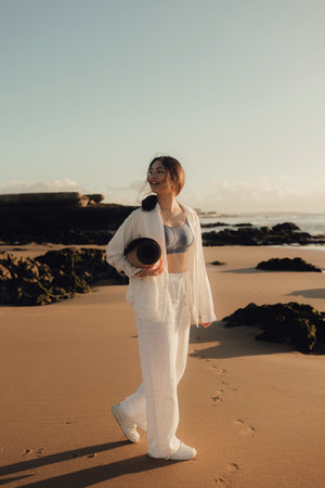 Asian happy woman in white clothes with yoga mat on the ocean shore. Concept of health exercises and yoga. Tourism alone. Part of series.の写真素材