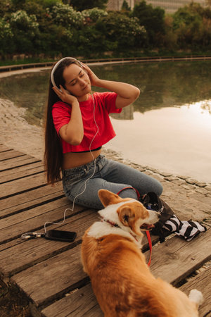 Close-up of a woman with Welsh Corgi in a park on a hot sunny day. The dog looks tired from the heat. Concept of summer walk, pet care, and companionship. Soft focus. Part of a series.の写真素材
