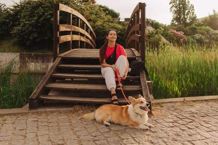 Close-up of a woman with Welsh Corgi in a park on a hot sunny day. Concept of pet care and companionship. Dog walker. Woman with her pet have fun at morning walking. Soft focus. Part of a series.の写真素材