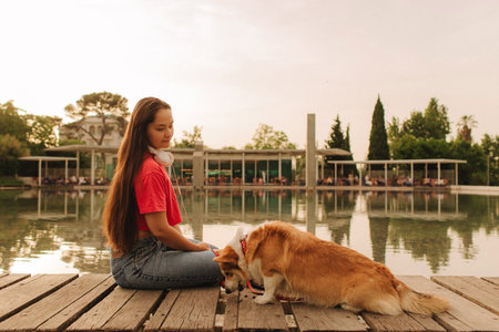 Close-up of a woman with Welsh Corgi in a park on a hot sunny day. The dog looks tired from the heat. Concept of summer walk, pet care, and companionship. Soft focus. Part of a series.の写真素材