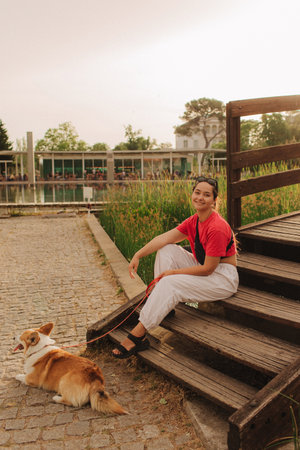 Close-up of a woman with Welsh Corgi in a park on a hot sunny day. Concept of pet care and companionship. Dog walker. Woman with her pet have fun at morning walking. Soft focus. Part of a series.の写真素材
