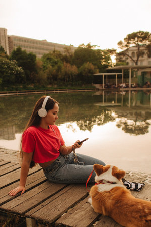 Close-up of a woman with Welsh Corgi in a park on a hot sunny day. The dog looks tired from the heat. Concept of summer walk, pet care, and companionship. Soft focus. Part of a series.の写真素材