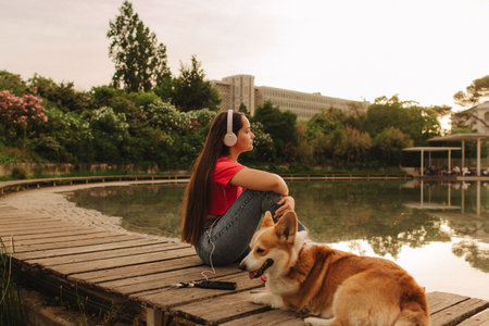 Close-up of a woman with Welsh Corgi in a park on a hot sunny day. The dog looks tired from the heat. Concept of summer walk, pet care, and companionship. Soft focus. Part of a series.の写真素材