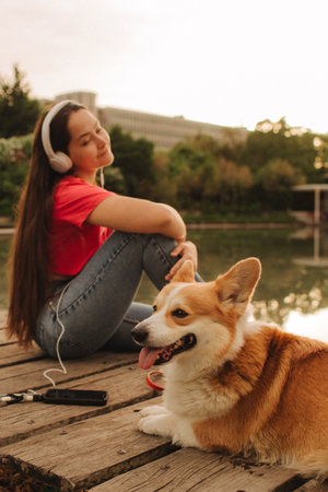 Close-up of a woman with Welsh Corgi in a park on a hot sunny day. The dog looks tired from the heat. Concept of summer walk, pet care, and companionship. Soft focus. Part of a series.の写真素材
