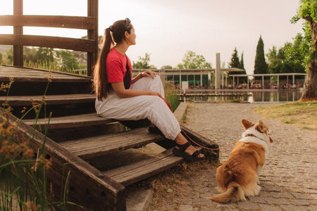 Close-up of a woman with Welsh Corgi in a park on a hot sunny day. Concept of pet care and companionship. Dog walker. Woman with her pet have fun at morning walking. Soft focus. Part of a series.の写真素材