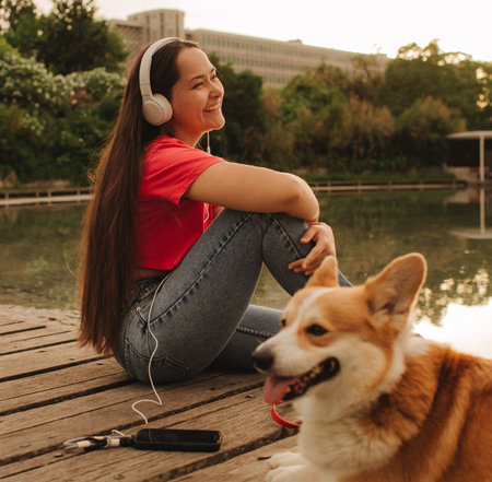 Close-up of a woman with Welsh Corgi in a park on a hot sunny day. The dog looks tired from the heat. Concept of summer walk, pet care, and companionship. Soft focus. Part of a series.の写真素材