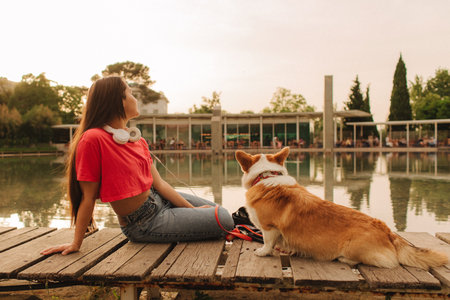 Close-up of a woman with Welsh Corgi in a park on a hot sunny day. The dog looks tired from the heat. Concept of summer walk, pet care, and companionship. Soft focus. Part of a series.の写真素材