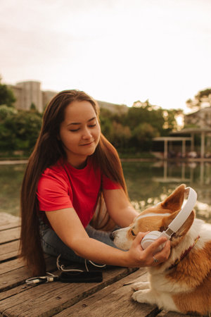 Close-up of a woman with Welsh Corgi in a park on a hot sunny day. The dog looks tired from the heat. Concept of summer walk, pet care, and companionship. Soft focus. Part of a series.の写真素材