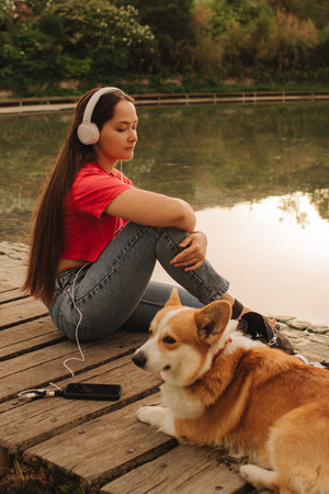 Close-up of a woman with Welsh Corgi in a park on a hot sunny day. The dog looks tired from the heat. Concept of summer walk, pet care, and companionship. Soft focus. Part of a series.の写真素材