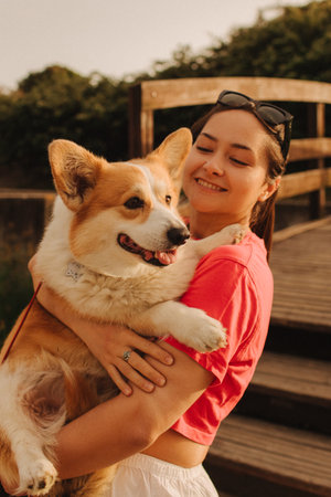 Close-up of a woman hugging a Welsh Corgi in the park in sunny weather. Concept of walking a dog, friendship between a dog and owner. Part of a series. Soft focus.の写真素材