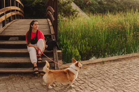 Close-up of a woman with Welsh Corgi in a park on a hot sunny day. Concept of pet care and companionship. Dog walker. Woman with her pet have fun at morning walking. Soft focus. Part of a series.の写真素材
