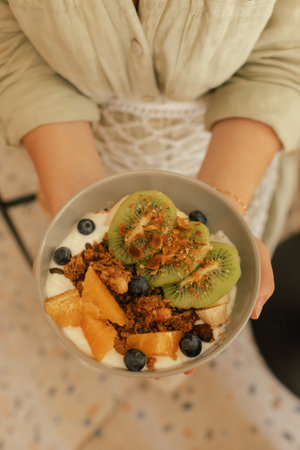 Close-up of female hands holding a plate. Granola with fresh fruit and yoghurt. A healthy natural...
