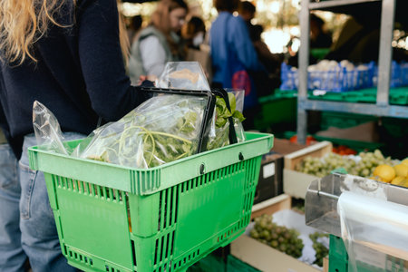 Close up of hand with a vegetables and greens in shopping basket on the local Farmers market. Mature Female Customer Shopping At Farmers Market Stall. Close up. Part of the series.の写真素材