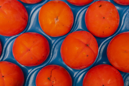 Fresh persimmon in plastic packaging at local urban market. Organic produce on sale at outdoor farmer market. Selling fresh crops and veggies harvest. European urban setting. Part of the seriesの写真素材