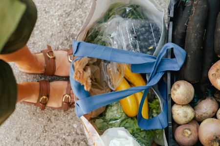 Close up of hand with vegetables and greens in shopping basket at the local Farmers market. Mature...