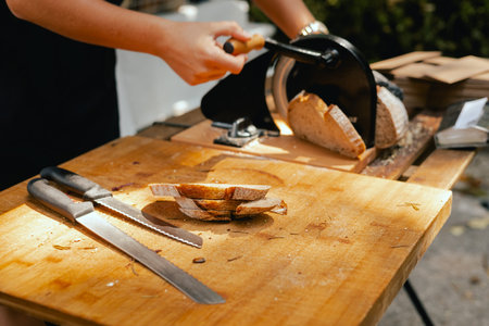 Hand-slicing craft bread on a table. The healthy eating and traditional bakery concept. Close up....