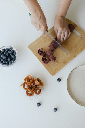 Caucasian woman preparing homemade fruit leather, slicing fresh fruit in her kitchen for a healthy...