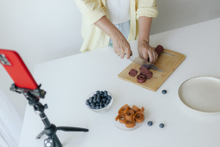 Middle-aged woman preparing homemade fruit leather, slicing fresh fruit in her kitchen for a healthy snack. Part of a series on organic treats and natural living. User-generated content.の写真素材