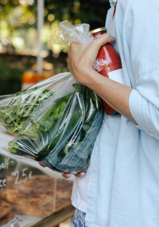 Close-up of female hands putting vegetables into a bag at a local market. Organic produce on sale at...