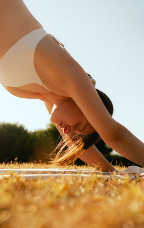 Young woman in sportswear stretching body on fitness mat at public park, doing yoga. Healthy lifestyle, sport. Fitness. Girl doing yoga in morning park. Part of a series.の写真素材