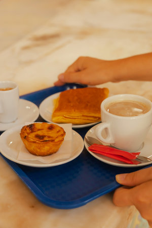 Close up middle age woman tries Portuguese egg tart pastry called Pastel de Nata with coffee near...